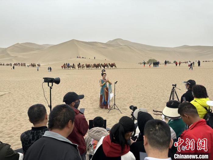 圖為2023年4月底，敦煌大漠“逐舞者”奧楠在鳴沙山月牙泉景區(qū)視頻直播，吸引游人圍觀?！●T志軍 攝
